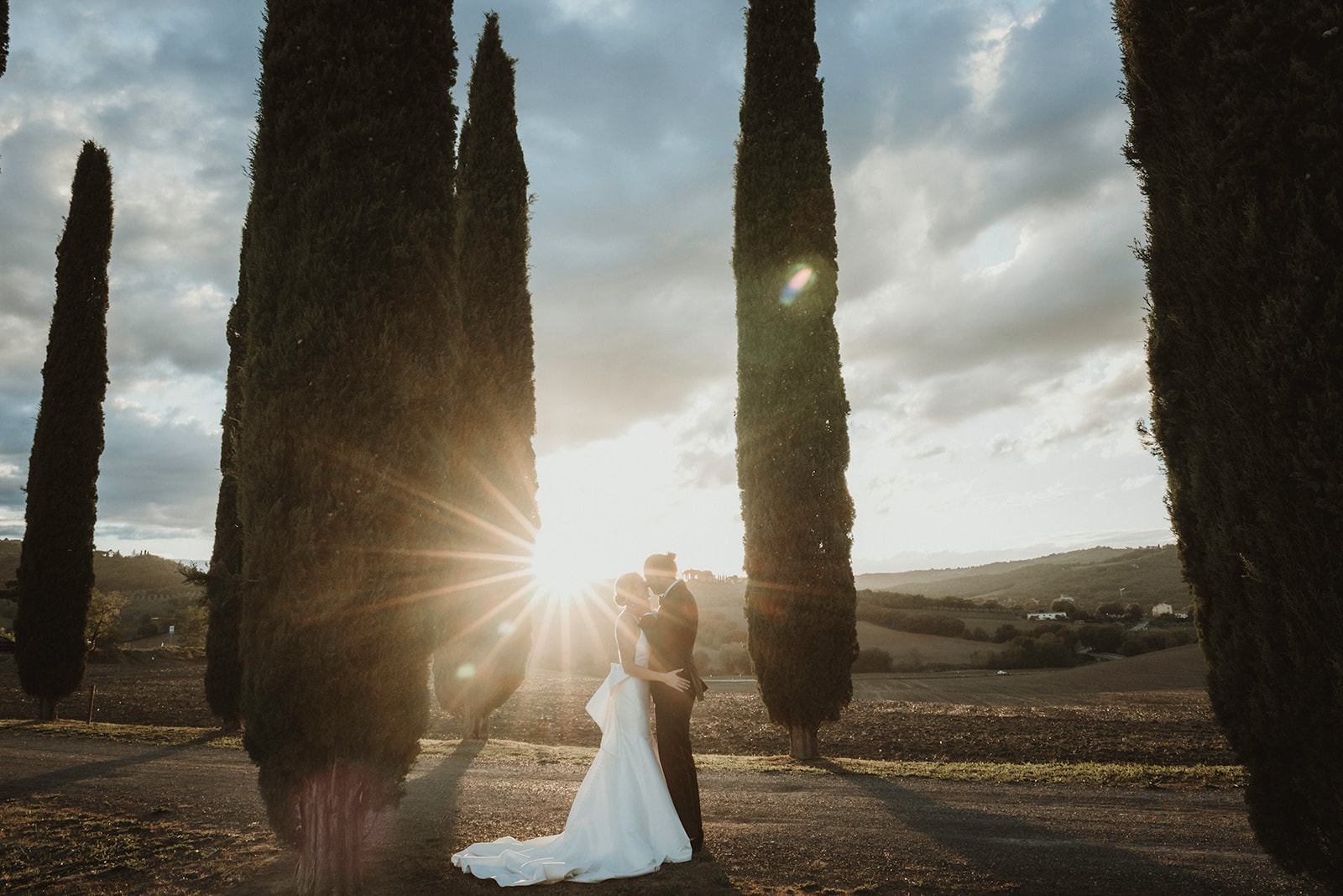 Couple kissing with the most dramatic sunset light within Cypresses in the Tuscan countryside on their elopement in Italy