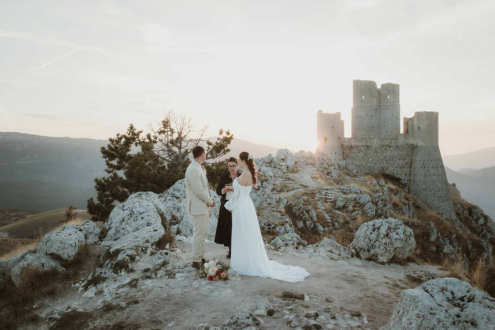 Couple on their symbolic ceremony at dawn in Central Italy on a rocky mountain with medieval castle in the background