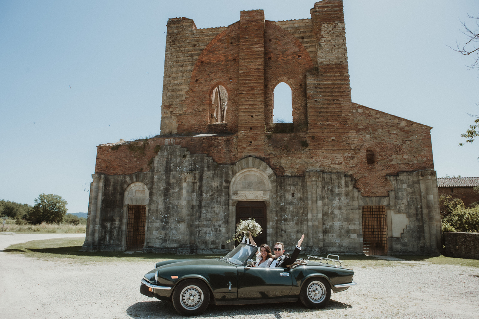 Bride and Groom in a vintage car in front of San Galgano, Italy for their elopement in Tuscany