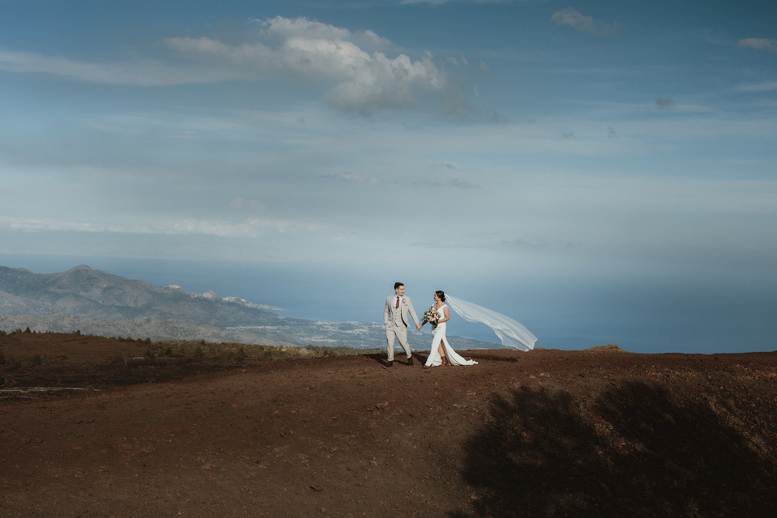 Couple walking on a volcanic ridge on Mount Etna with views of the sea and the bays on their elopement in Sicily