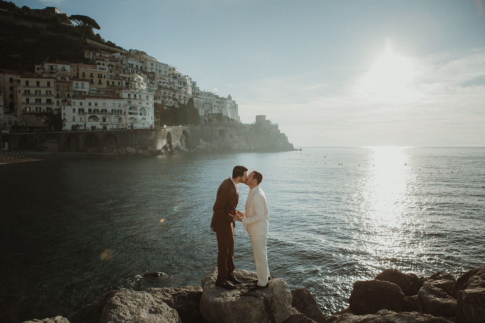 Queer couple kissing at dawn for their elopement in the Amalfi Coast with crystal clear water in the background