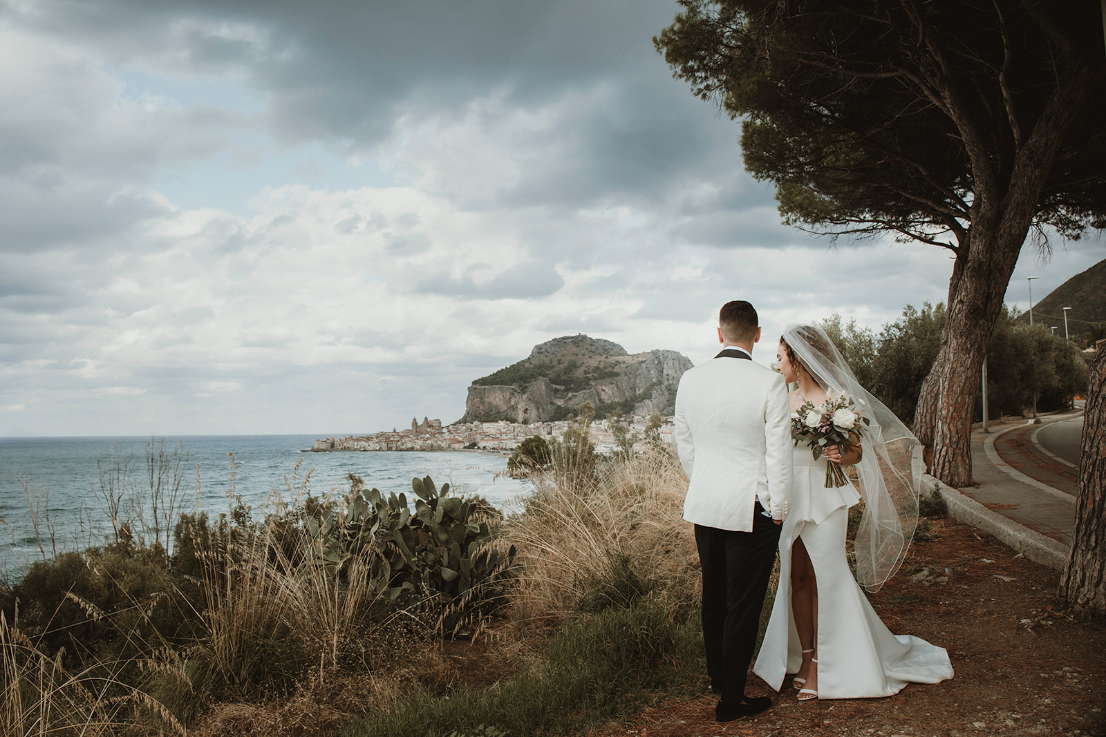 Couple posing candidly as they admire the views of Cefalù at the back on their elopement in Sicily