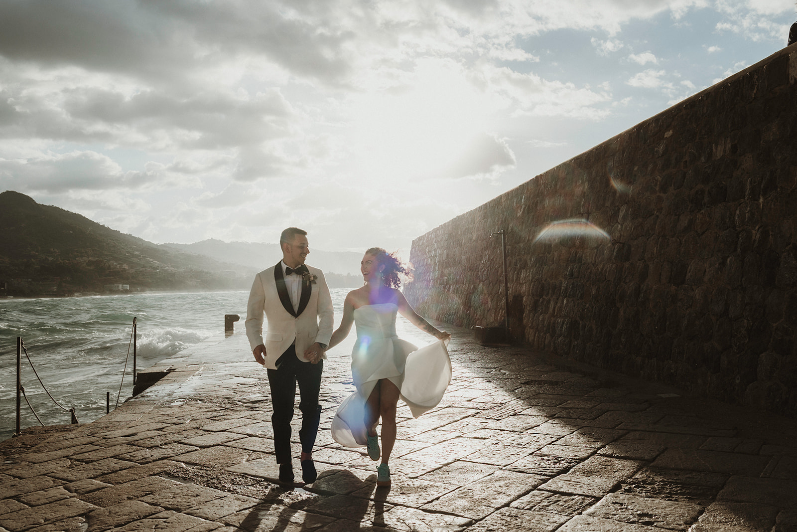 Couple running happily with dramatic sky and sea views on their elopement in Cefalù, Sicily