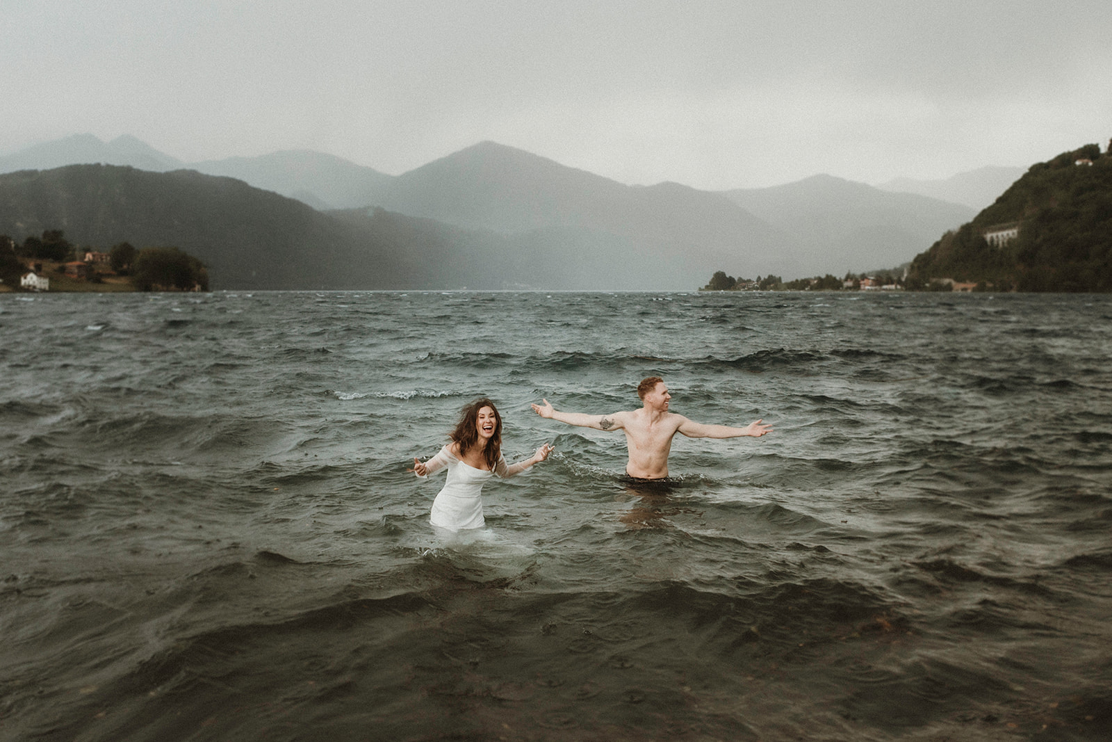 Adventure couple during a trash the dress moment laughing in the waters of Lake Orta as a storm is approaching on their Elopement in Italy