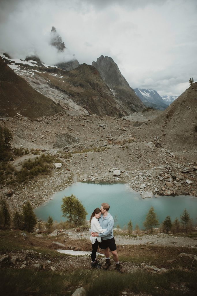 Couple standing beside a turquoise glacier lake with alpine peaks in the background during their Mont Blanc elopement experience.