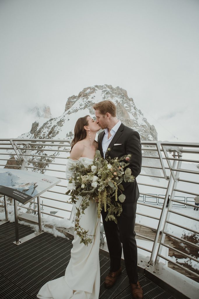 Bride and groom standing on snowy terrain at Punta Helbronner with dramatic Mont Blanc peaks behind them.