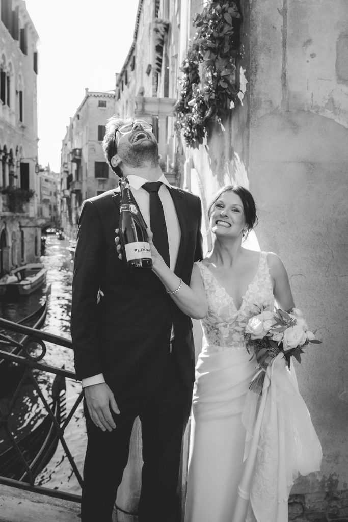 Fun picture of a couple with a bottle of Champagne happily celebrating their elopement in Venice