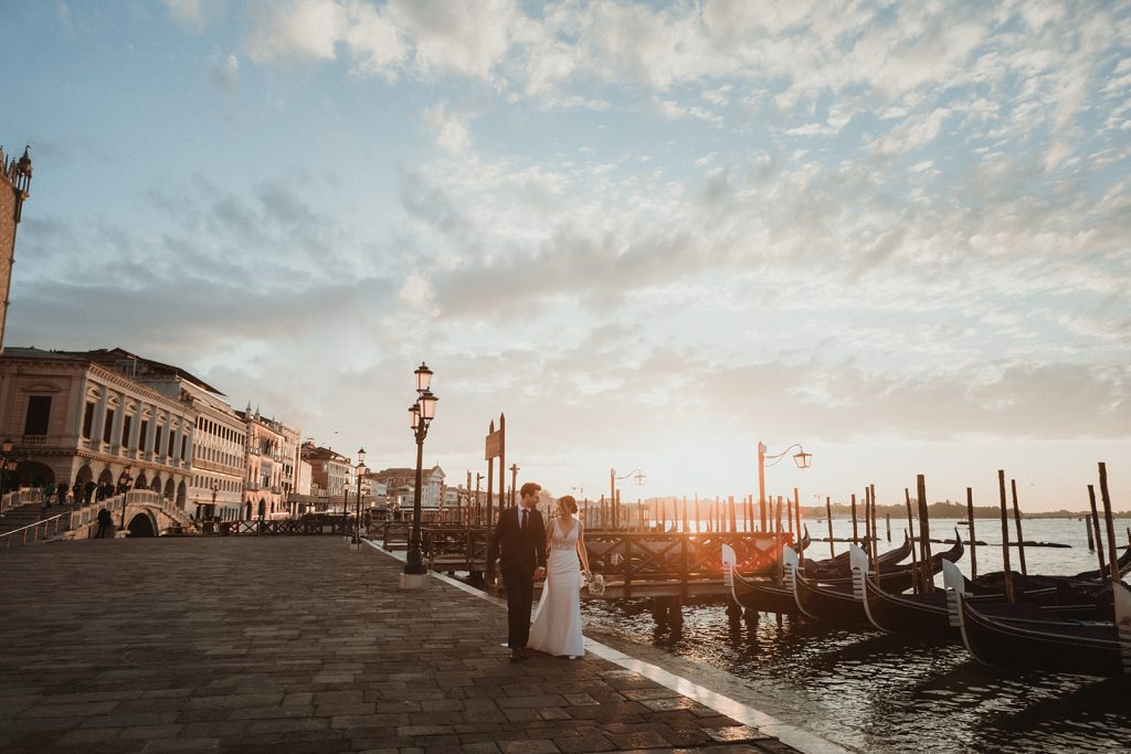 Couple walking at sunrise in Venice with golden light in the background, gondolas and water views