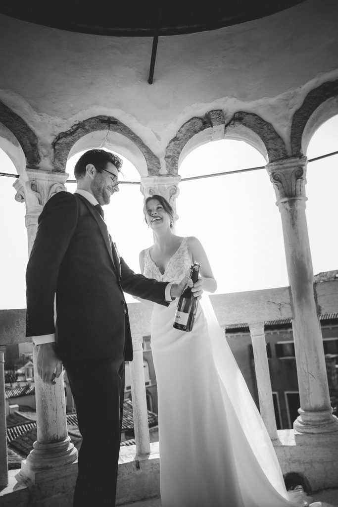 Couple popping a bottle of Champagne right after their symbolic ceremony at Palazzo Contarini del Bovolo