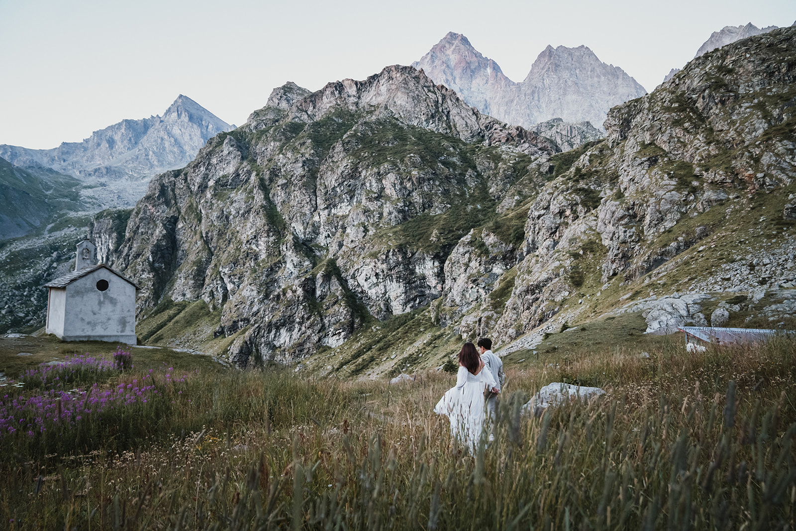 Couple hiking in their wedding attire in a mountain landscape, with rugged rocks and high peaks on their elopement in Italy