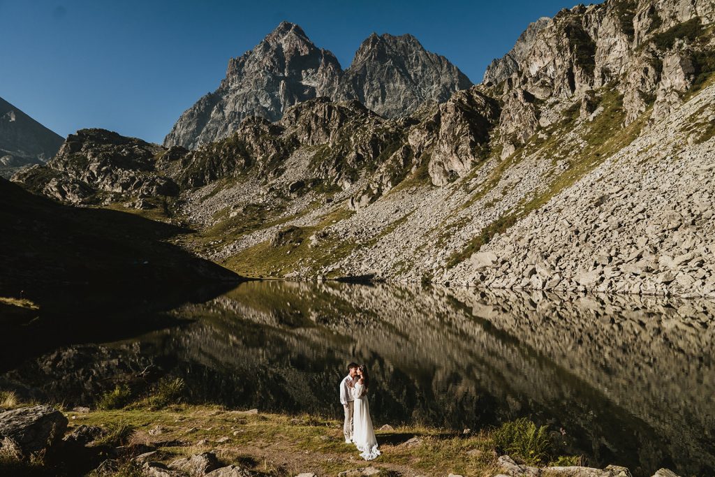 Couple embracing with mountain view in the backdrop and lake reflections on their mountain elopement in Italy