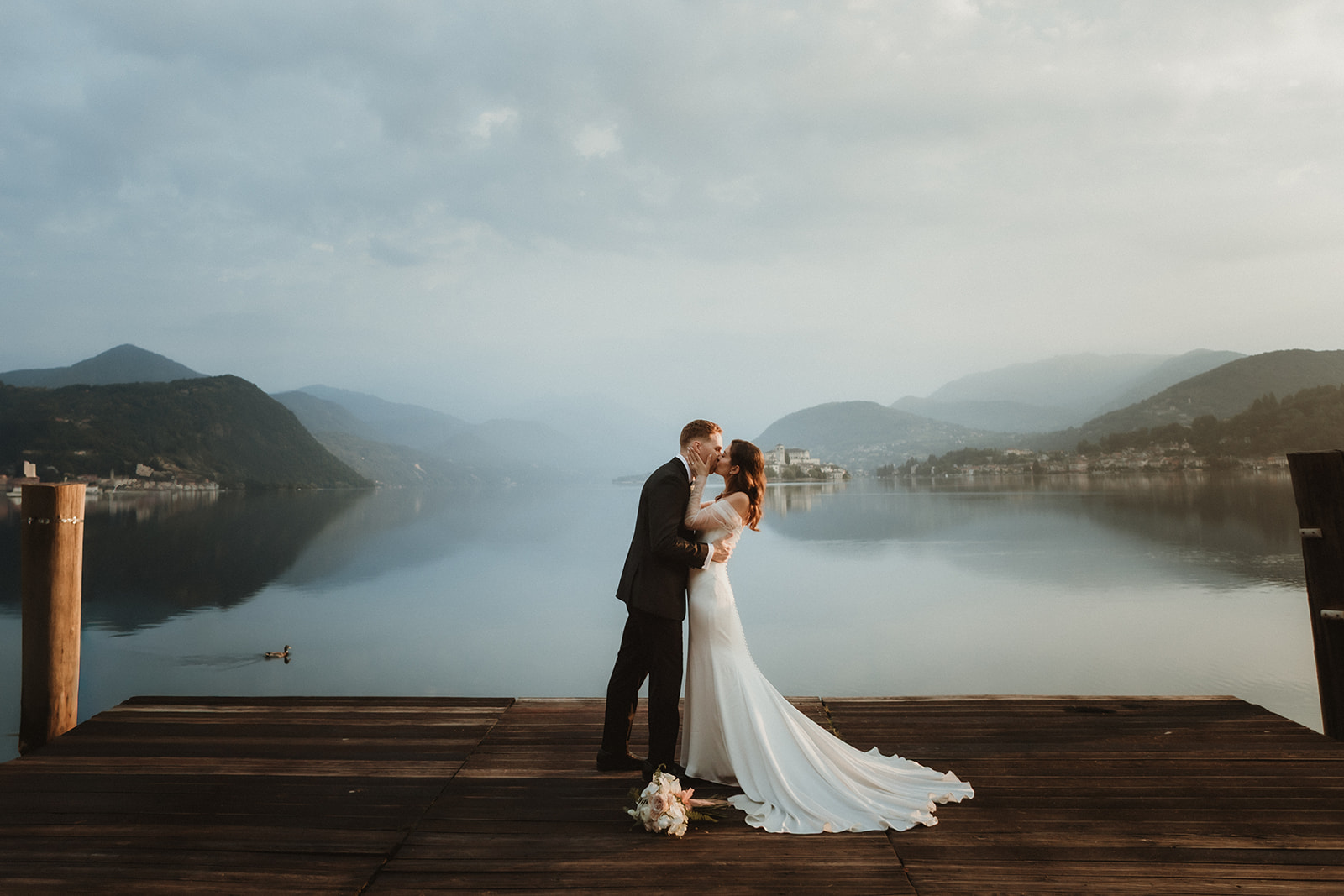 Couple kissing by the shores of a lake in Norther. Italy as dawn approches on their elopement day.
