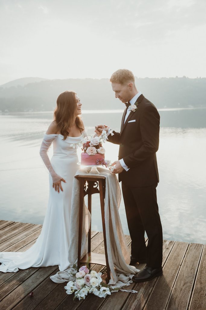 Couple cutting their wedding cake at sunrise by a Northern Italy lake on their elopement day.