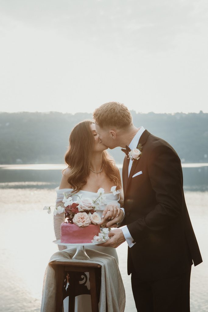 Couple cutting their wedding cake at sunrise by a Northern Italy lake on their elopement day.