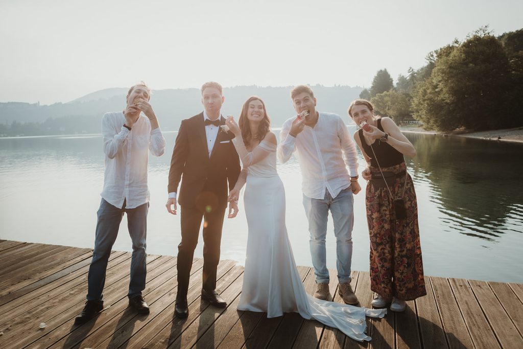 Couple eating their wedding cake at sunrise on the shores of the lake with the team that planned their Italy elopement