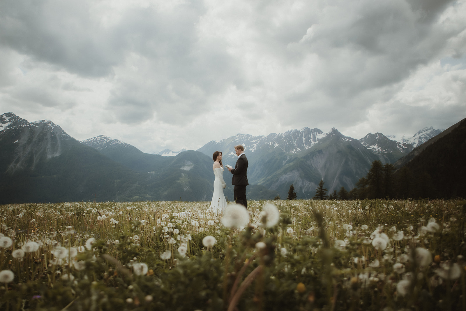 Couple exchanging vows in a meadow in the Italian Alps, surrounded by flowers in full bloom with high peaks in the backdrop.