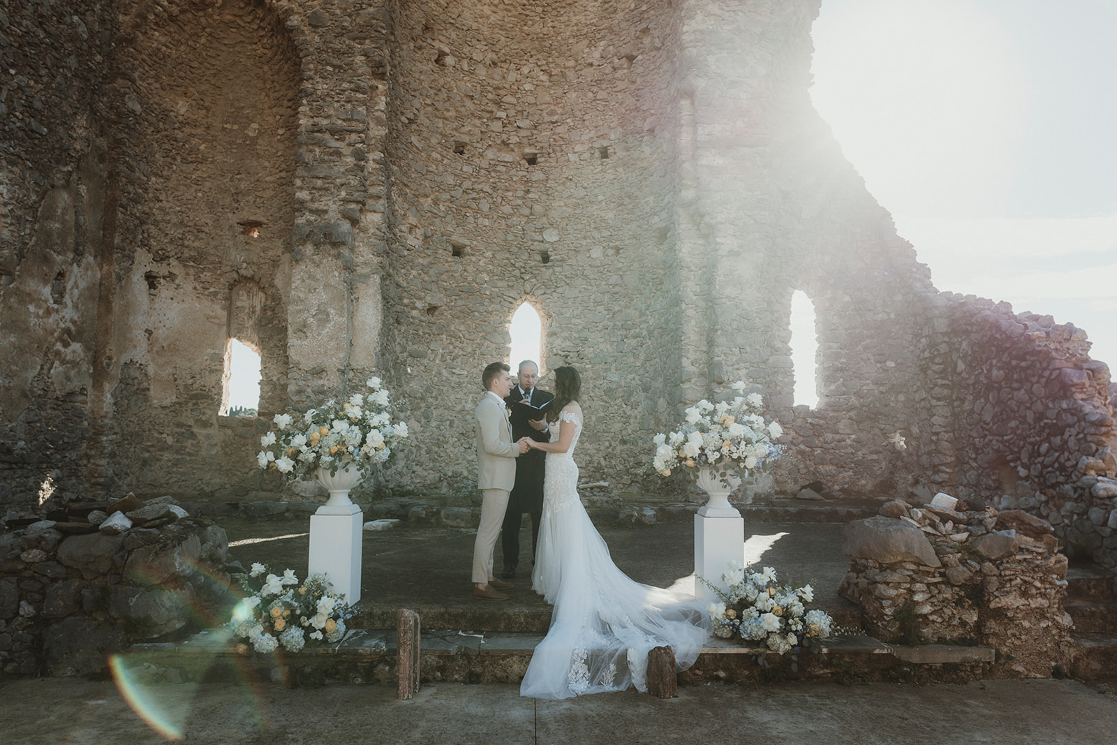 Couple exchanging vows with a celebrant in typical Italian ruins with sun in the background